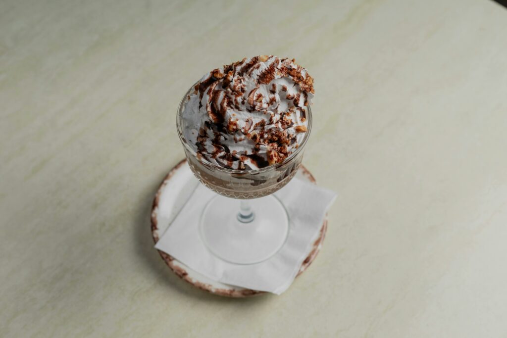 A tempting chocolate sundae with whipped cream in a vintage glass on a wooden surface.