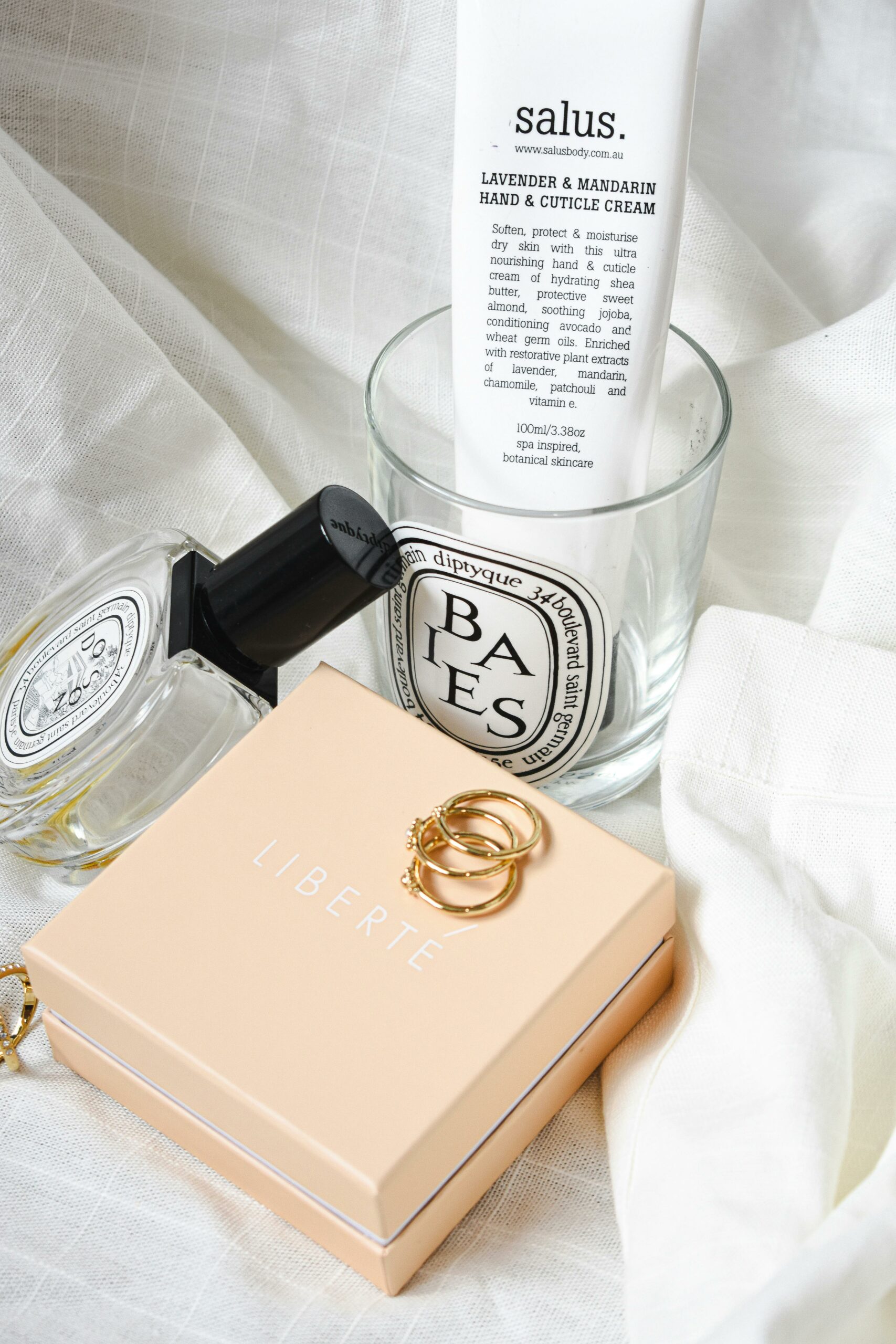 Sophisticated arrangement of cosmetics, jewelry, and cream on white fabric, showcasing elegance and style.