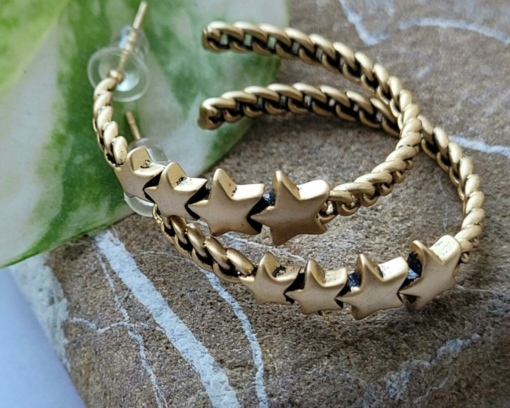 Close-up of gold star hoop earrings displayed on a textured stone with a touch of greenery.